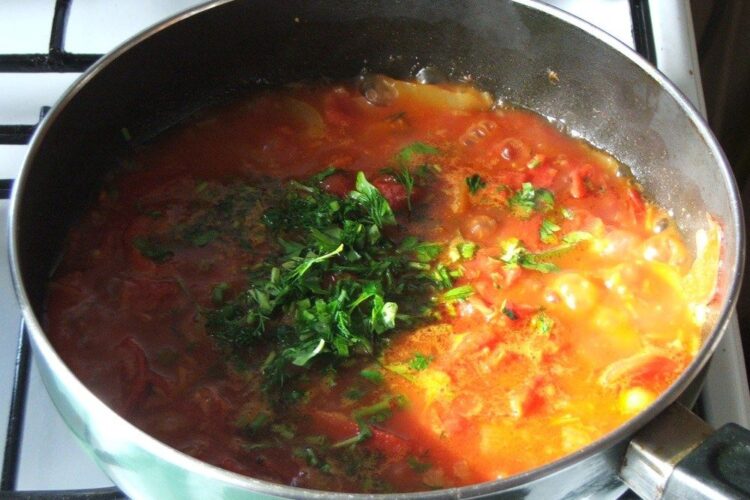 Adaugare verdeata in sosul de rosii pregatit pentru paste cannelloni umplute cu peste, in sos de rosii.