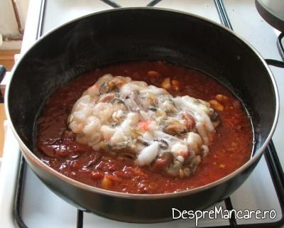 Creveti congelati adaugati in sos fierbinte de rosii pentru preparare biban cu creveti in sos de rosii.
