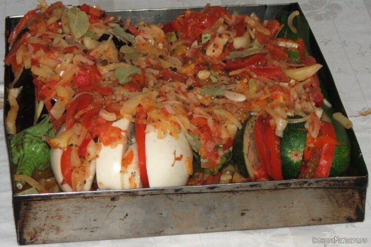 Vinete si dovlecei zimtate(i) impanate cu legume si acoperite cu legume calite, pregatite in tava pentru introdus la cuptor.